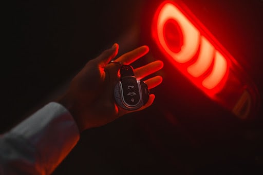 Someone holding a car key fob in front of an illuminated brake light.