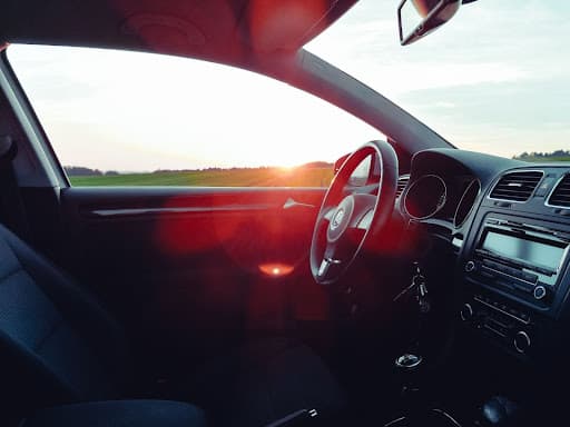 A car’s interior dashboard and steering wheel in a sunset. 