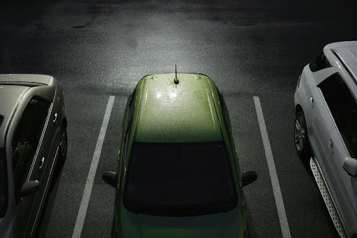 A green car parked in a space in a dark parking lot.