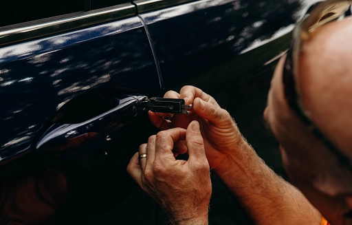 A man trying to unlock a car door with a device.