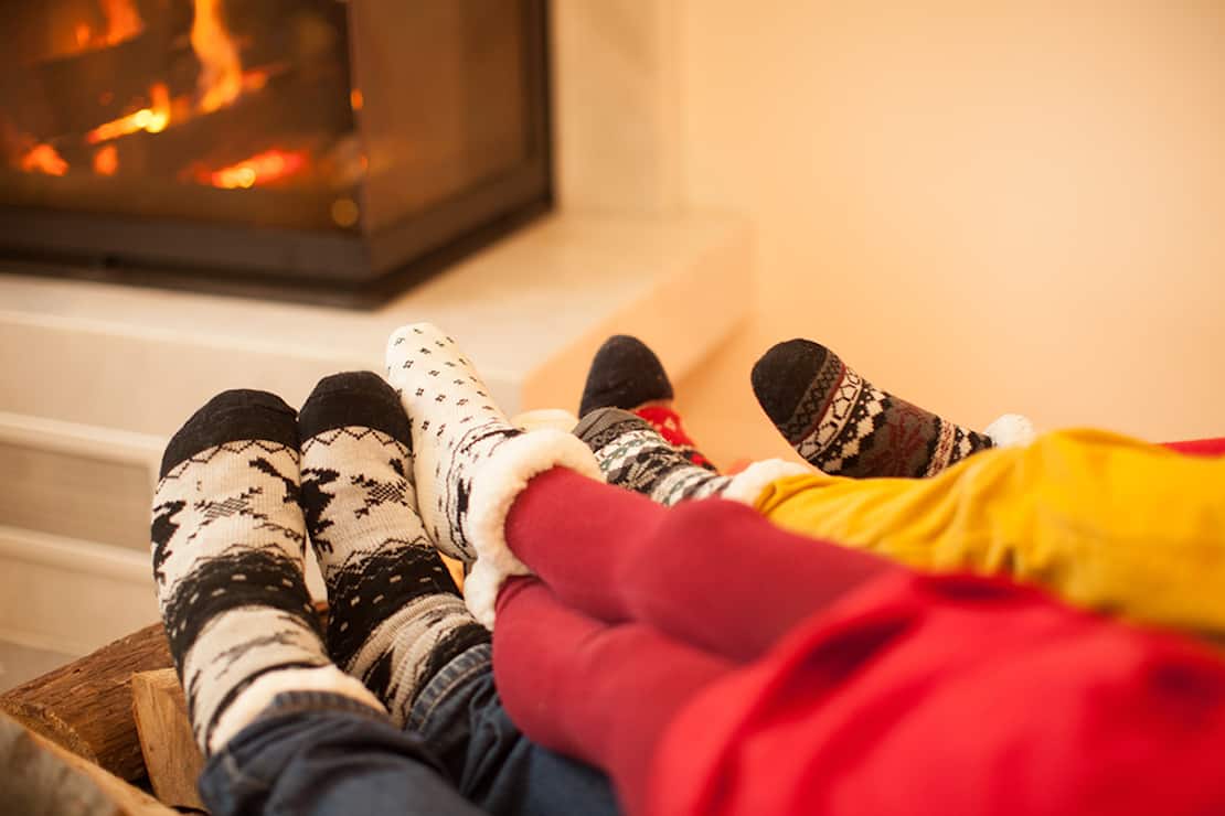 Three people's sock-clad feet held out to the fireplace.