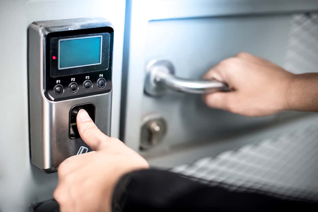 Person holding their thumb on a keypad to unlock a door.