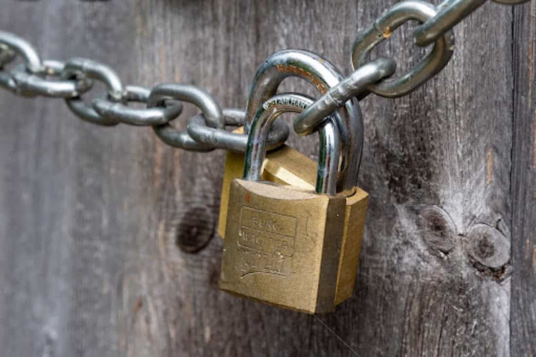 Padlock connecting a chain on a wooden fence.