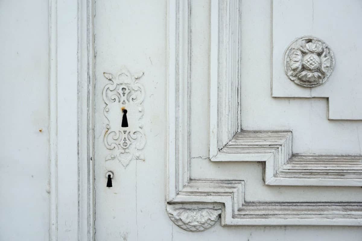White-painted lock on a white door with ornate detailing.