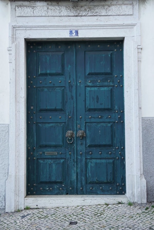 A set of teal double doors with iron lion shaped knockers.
