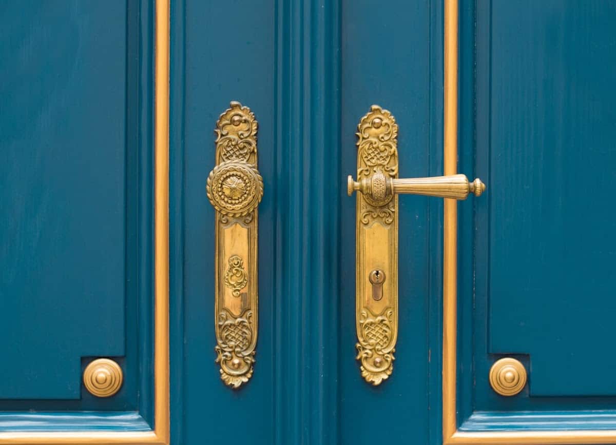 Gold plated doorknobs on teal doors with gold accents.