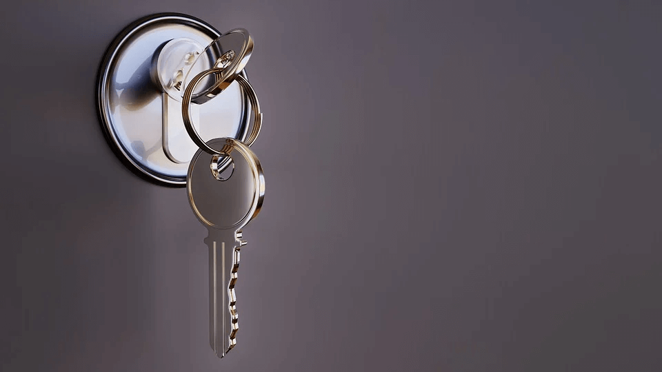 Keys dangling from a lock on a grey door.