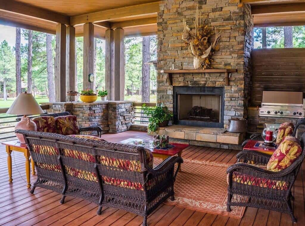 Cozy porch with wicker couch and chairs in front of a stone fireplace.
