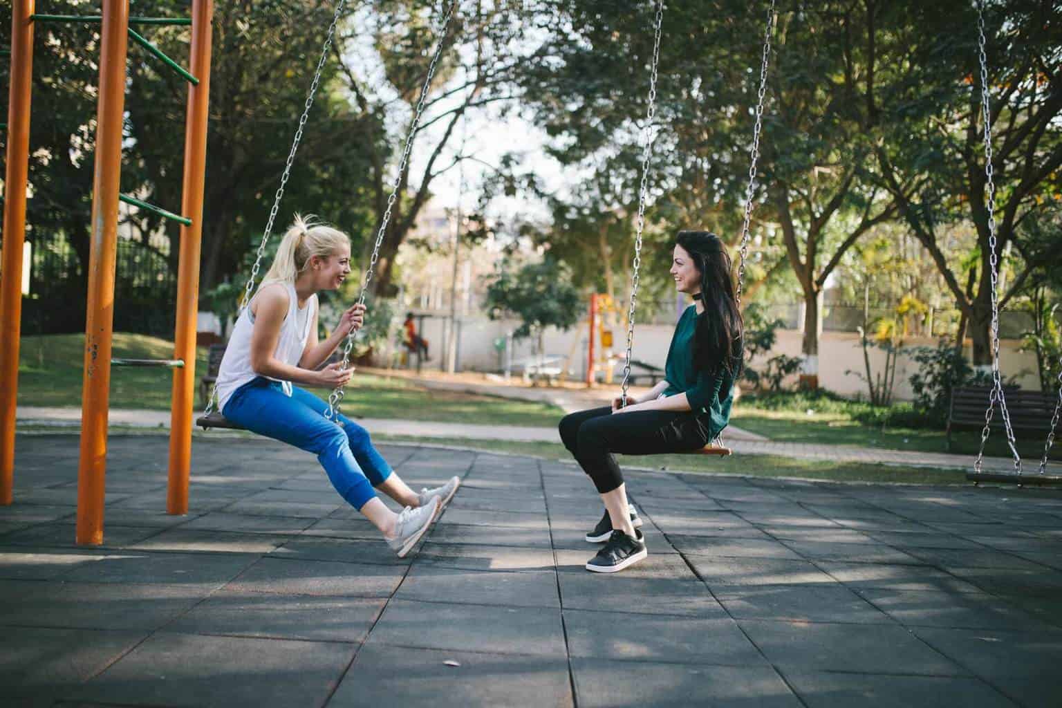 Two people sitting on swings facing each other.