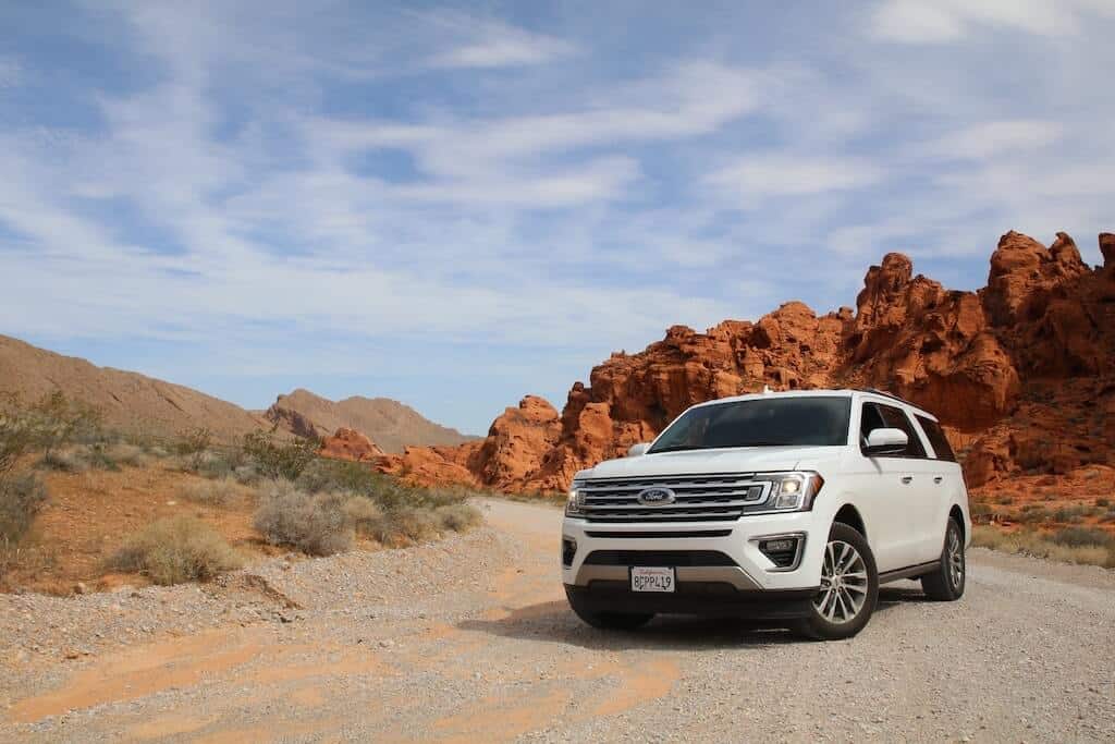 White SUV on a dirt road in front of mountains.