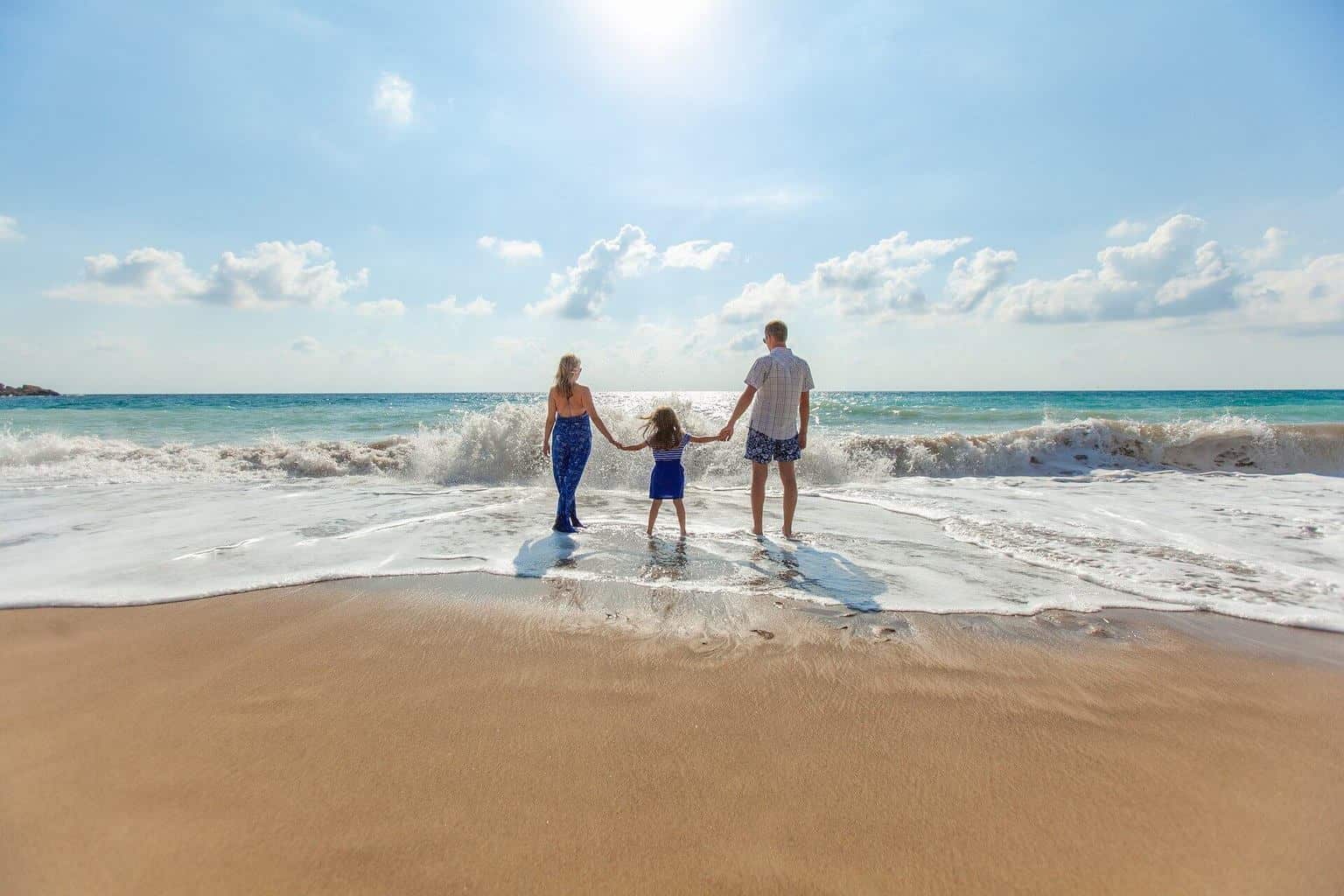 Family of three holding hands on the beach walking toward the water.