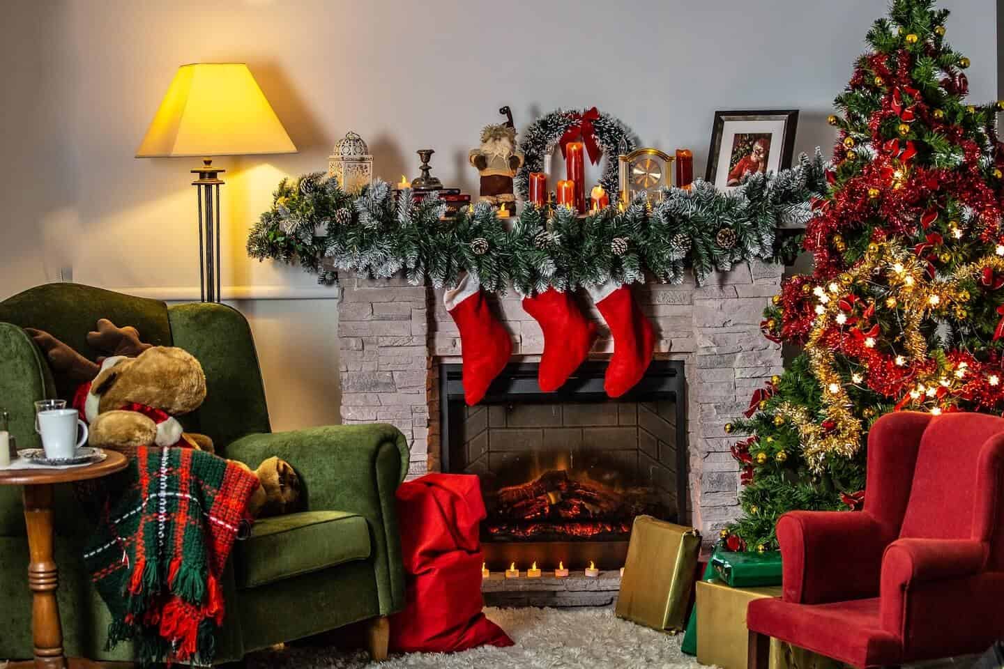 A living room decorated for Christmas, with red stockings hanging over a white fireplace next to a green armchair.