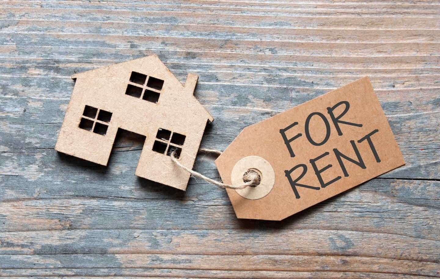 Cardboard facade of a house with a gift tag reading 'For Rent' looped through the window.