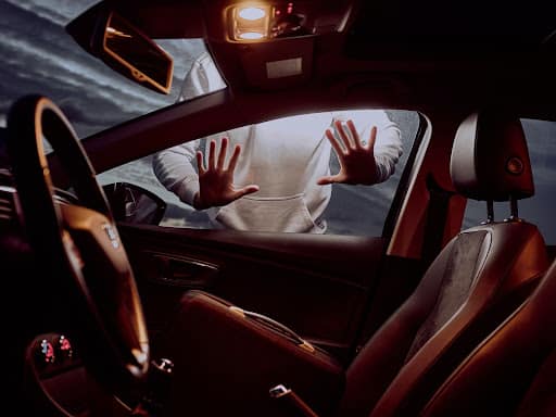 A person’s hands pressed against the outside of a car window. No one is inside the car, but the lights are on.  