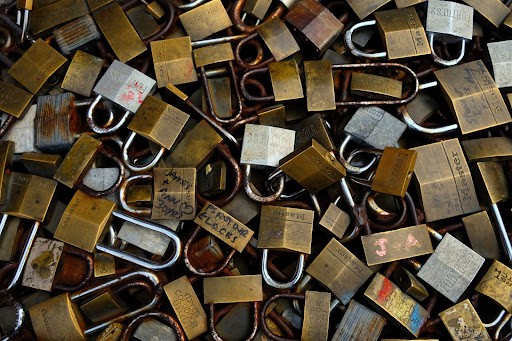 A large pile of padlocks in different shapes and sizes with names or other markings on some of them.