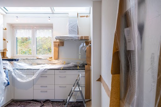 A photo of a kitchen area being remodeled with tarps and construction products. 