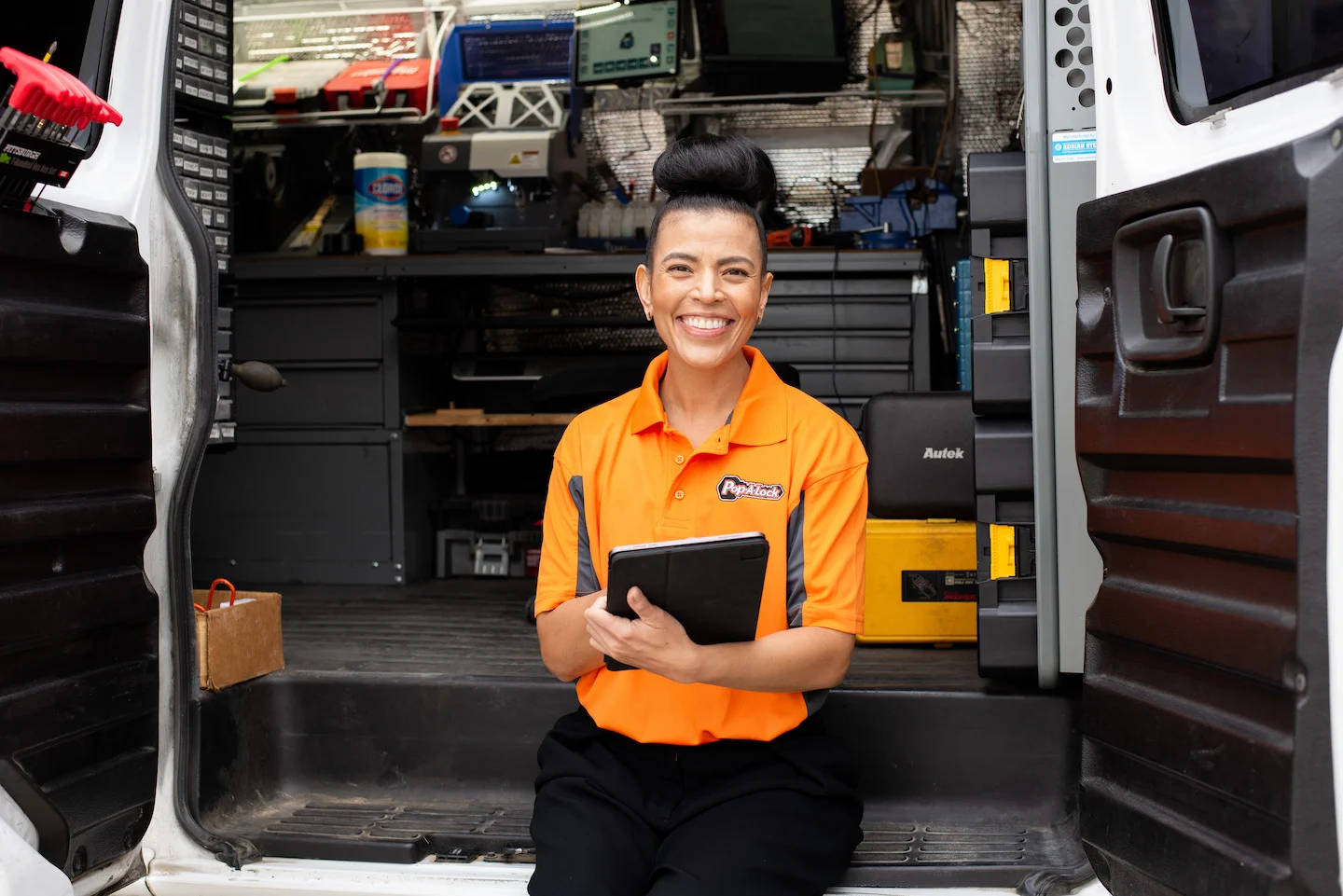 Locksmith technician sitting inside a locksmithing van while holding an ipad and smiling.