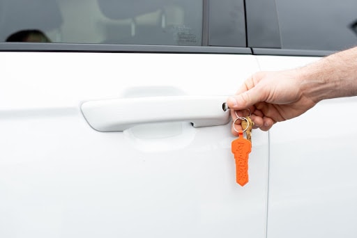 Person unlocking the door to their car. Their keys have an orange Pop-A-Lock keychain attachment.