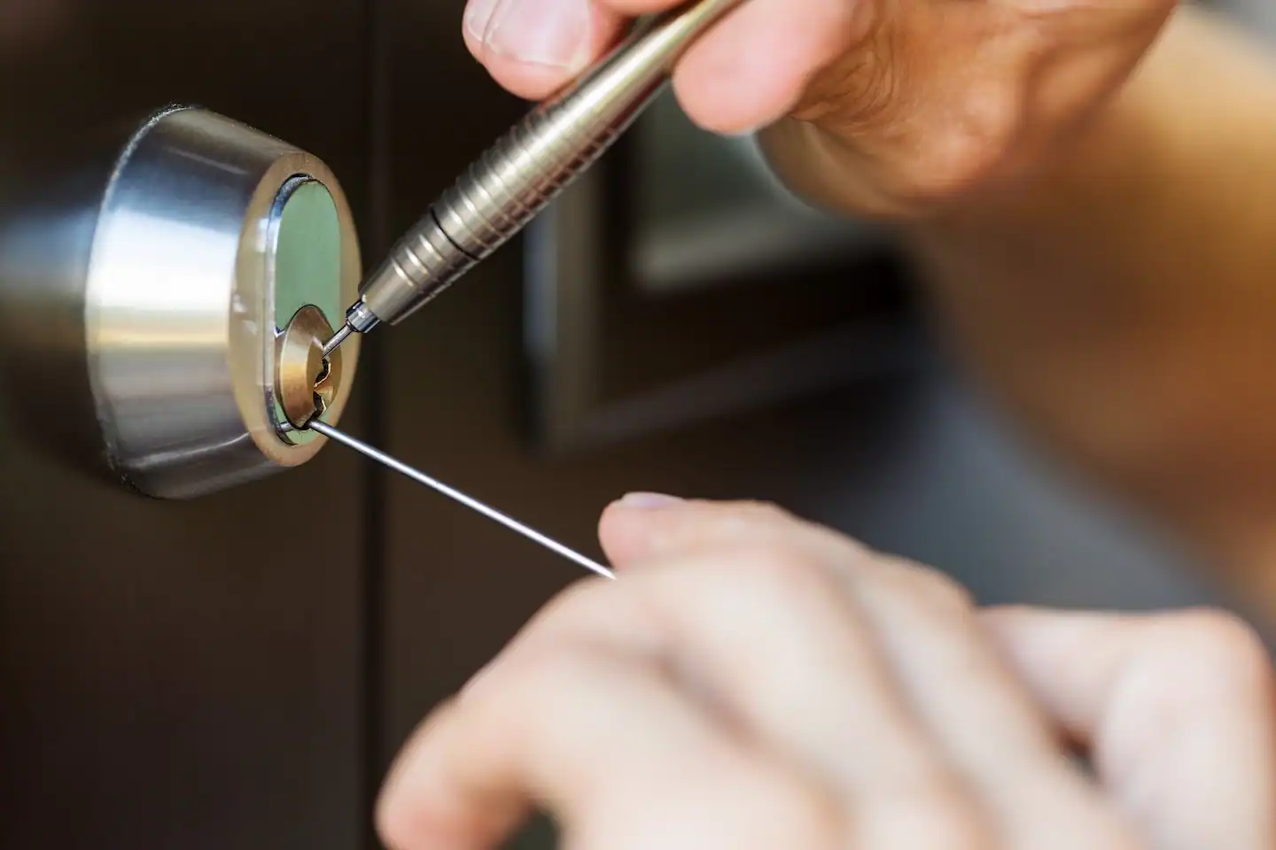 Closeup of a locksmith using pick tools to open a locked door.

